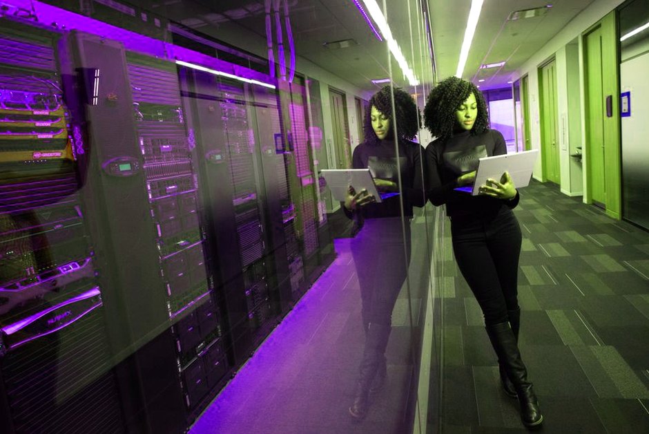 Femme sur un ordinateur portable dans un datacenter aux serveurs en miroir.